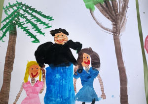 Na rysunku po prawej i lewej stronie narysowane są drzewa. Pomiędzy nimi babcia w niebieskiej spódnicy i czarnej bluzce trzyma za ręce dwie wnuczki. Jedna z brązowymi włosami i w niebieskiej sukience, druga z żółtymi włosami w różowej sukience.